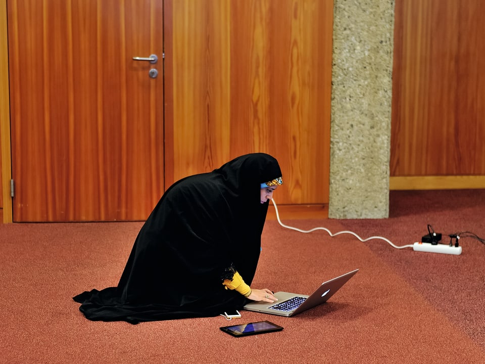 Eine iranische Fernsehjournalistin kniet an der Atomkonferenz in Genf von vergangenem November am Boden, vor ihr der Laptop, das Tablet und das Smartphone. Sie wartet auf ihren Einsatz in den Medien im Iran.