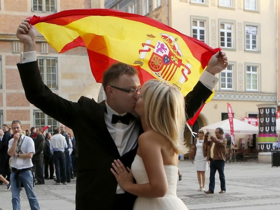 Ein Brautpaar küsst sich, im Hintergrund die spanische Flagge.