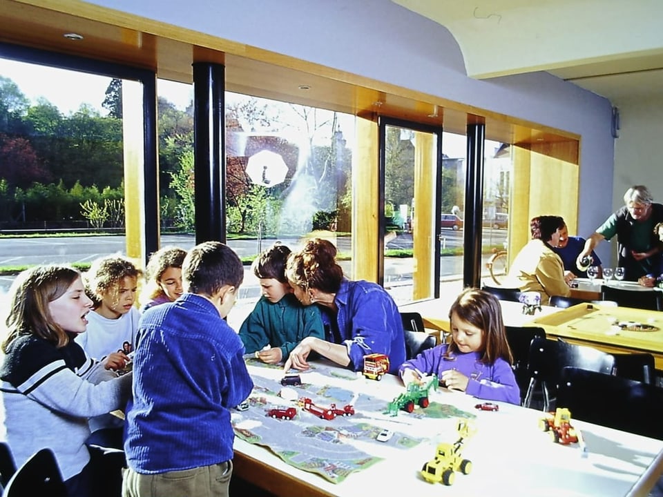 Gruppe von Kindern und Erwachsenen bei Bastelaktivitäten in einem hellen Raum mit grossen Fenstern