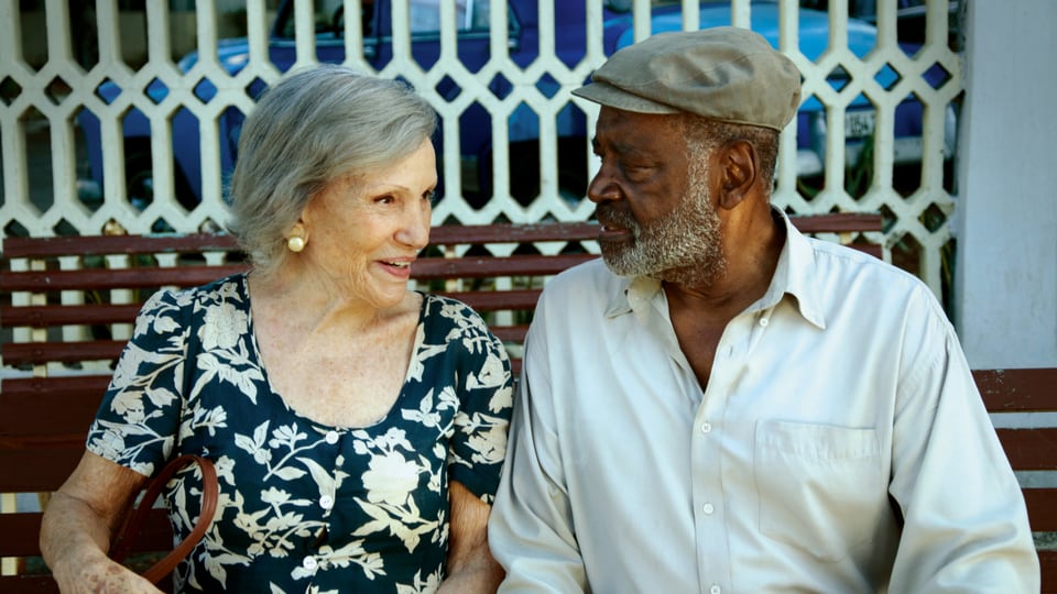 Das ältere Paar sitzt auf einer Bank und lacht zusammen.