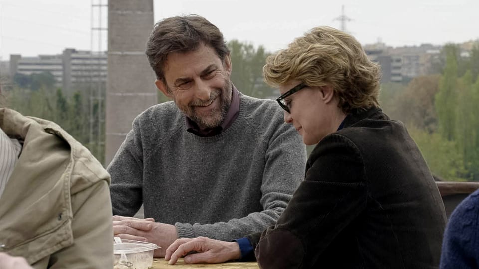 Ein Mann und eine Frau an einem Tisch sitzend, verhalten lachend im Gespräch.