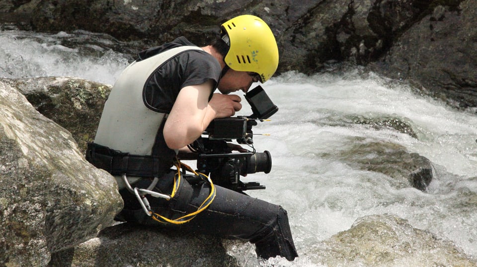Kameramann ist bis zu den Waden im Wasser während er filmt. 