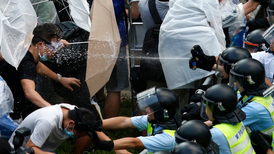 Polizisten gehen mit Pfefferspray gegen Demonstranten vor, die sich mit Regenschirmen wehren.
