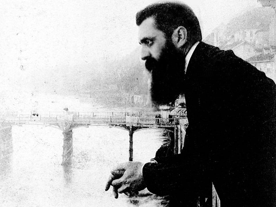 Ein Mann mit Bart steht auf dem Balkon am Rhein und schaut in die Ferne.