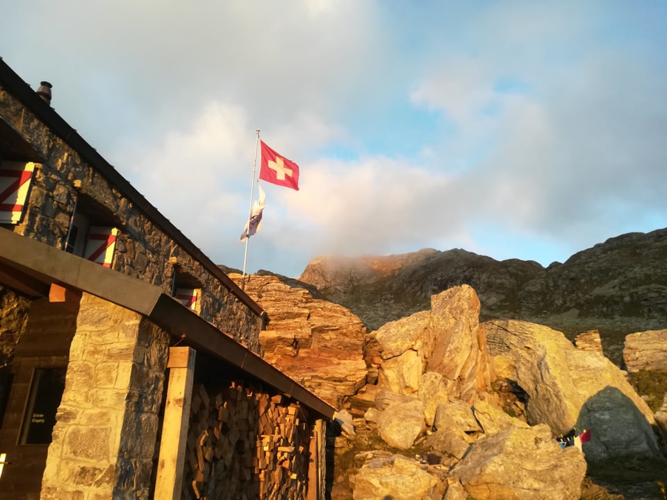 Eine Hütte im Nebel, dahinter eine Schweizer Fahne im Wind.