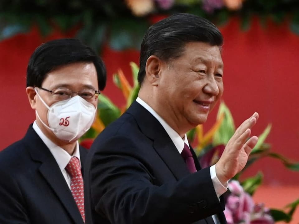Xi Jinping winkt dem Publikum zu. Hinter ihm steht John Lee.
