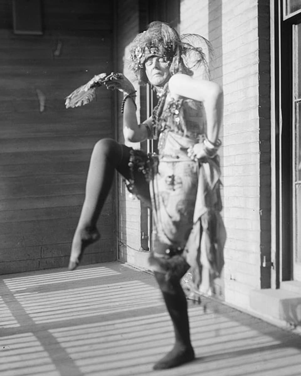 Eine Frau mit Federhut tanzt auf einem Bein.