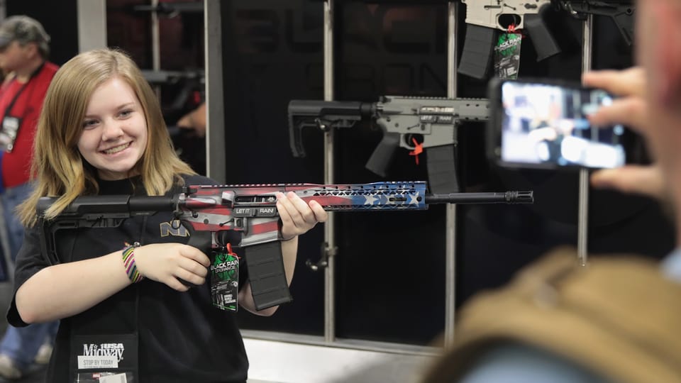 Ein Mädchen posiert mit einer Waffe. 
