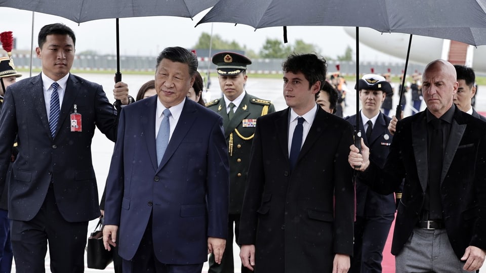 Diplomatische Delegation geht unter Regenschirmen, geführt von einem asiatischen Politiker.