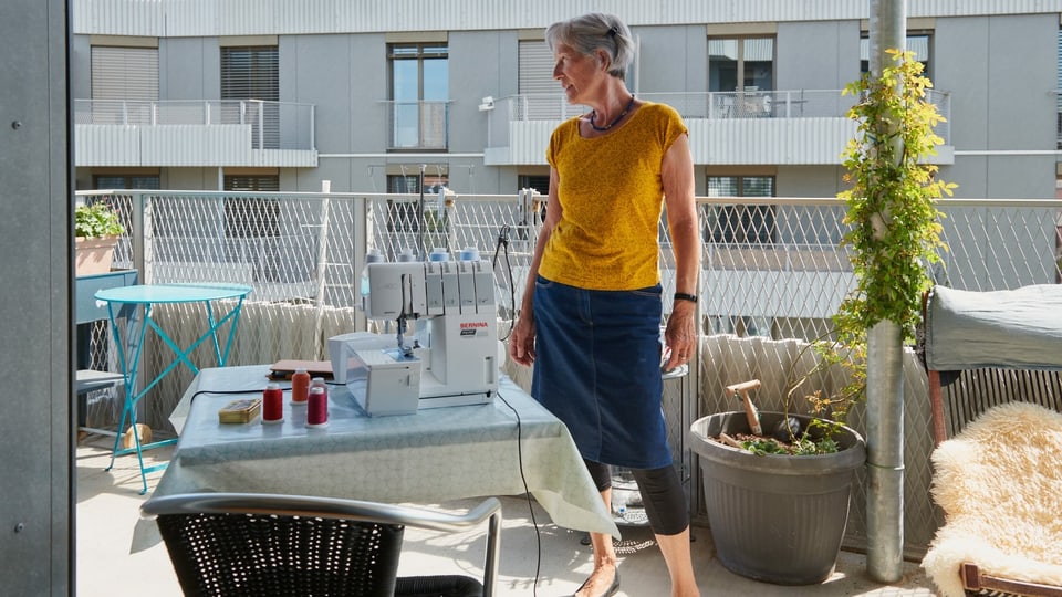 Eine ältere Frau auf dem Balkon mit Nähmaschine.