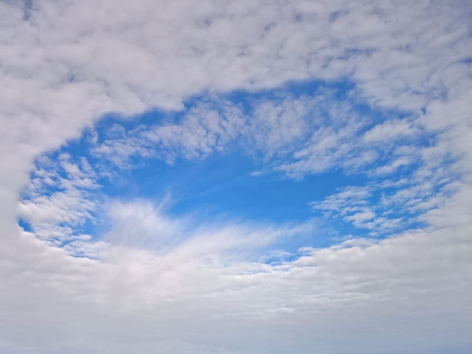Wolkendecke mit rundem, blauem Loch. Unten feine Eiskristallfasern. 
