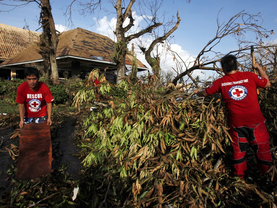 Etwas weiter entfernen zwei Helfer des philippinischen Roten Kreuzes umgestürzte Bäume vom Areal eines Strandhotels.