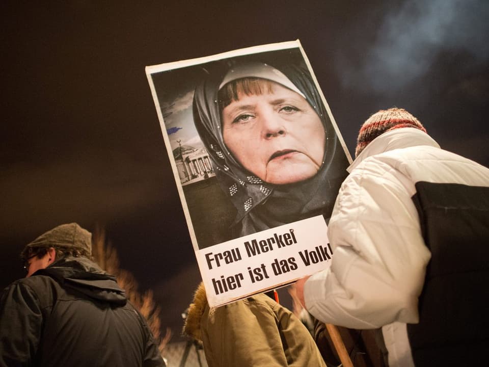 Jemand trägt ein Bild Merkels mit den Worten «Frau Merkel, hier ist das Volk.»