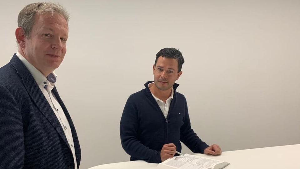 Zwei Herren stehen an einem Tisch. Vor ihnen ist ein Gesetzbuch aufgeschlagen.