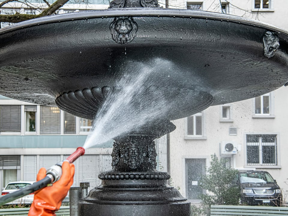 Hand hält Schlauch und spritzt Brunnen ab