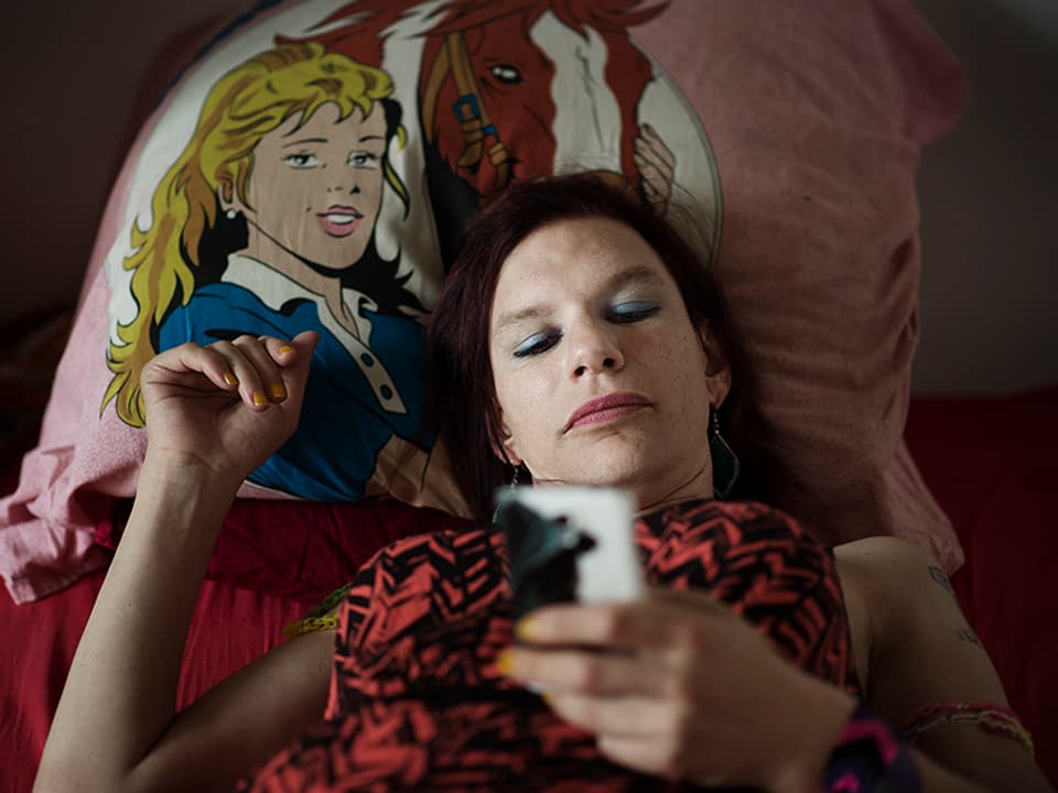 Eine Frau liegt auf dem Bett, in der Hand hält sie ein Handy. 