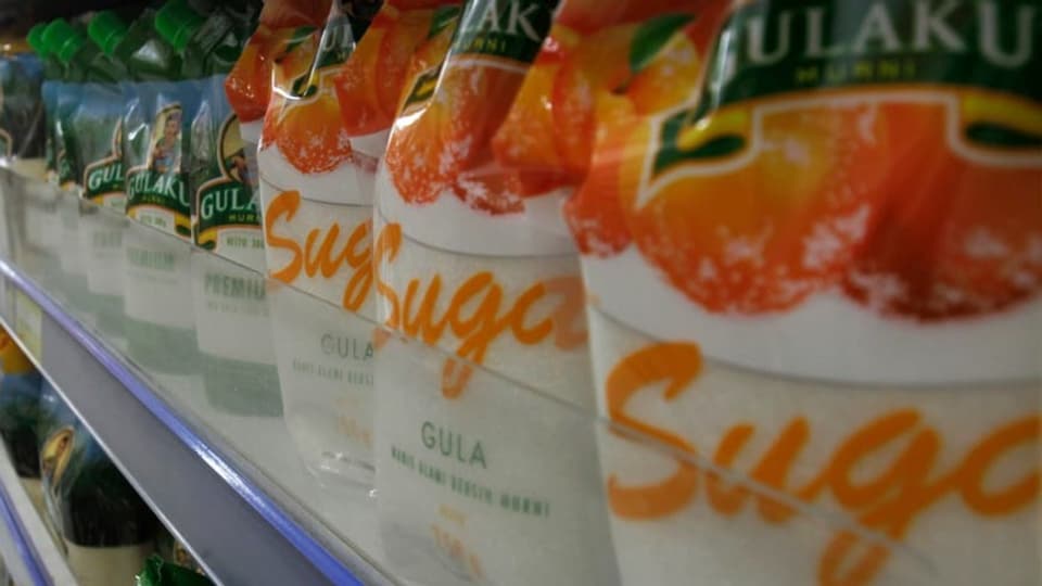 In einem Supermarkt stehen Zuckerpackungen in Regalen.