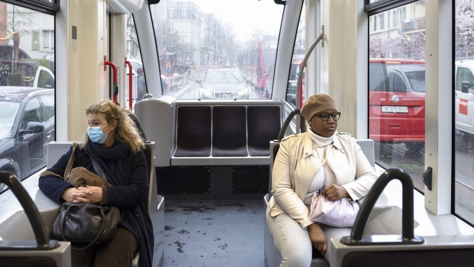 Zwei Passagiere in einem Bus, eine Frau trägt eine Maske.