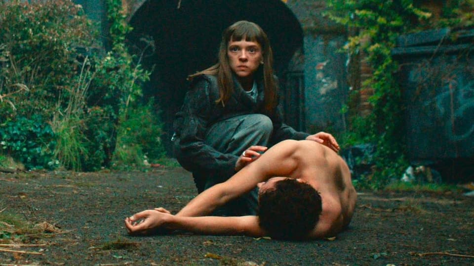 eine Frau kniet neben einem nackten, toten Mann.