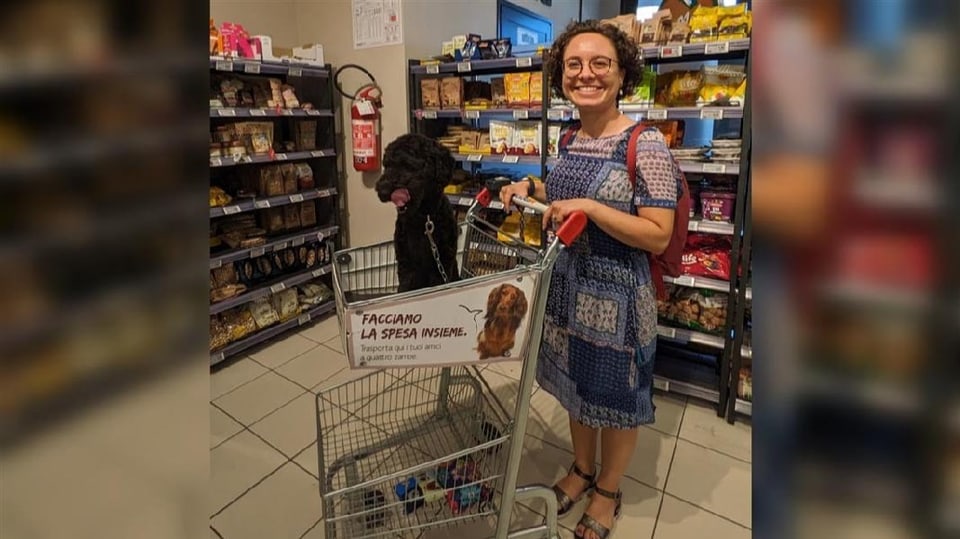 Hundebesitzerin in einem italienischen Laden mit Einkaufswagen und Hund darin.