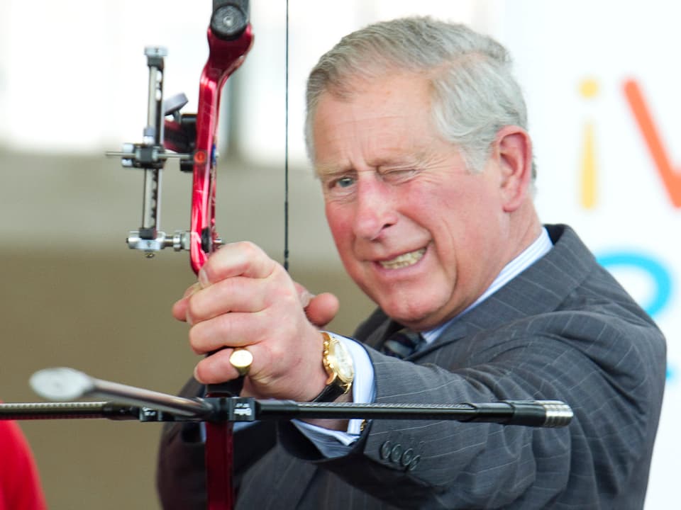 Prinz Charles mit einem Bogen in der Hand zielend.