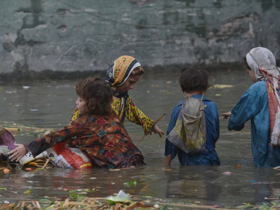 Bewohner von Badami Bagh auf ihrem Weg durch die überschwemmten Strassen.