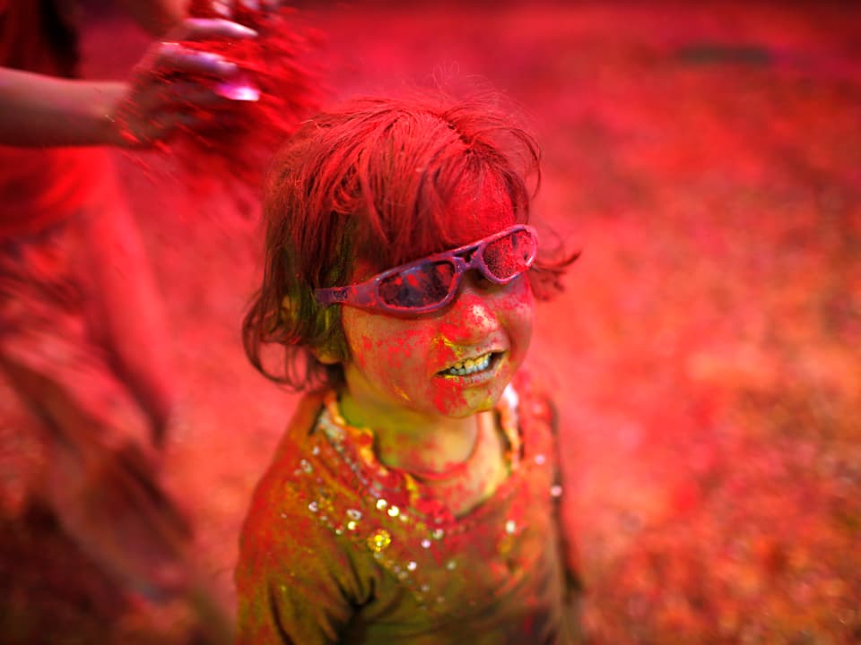 Ein Kind mit einer Sonnenbrille ist mit verschiedenen Farbpulvern verschmiert.