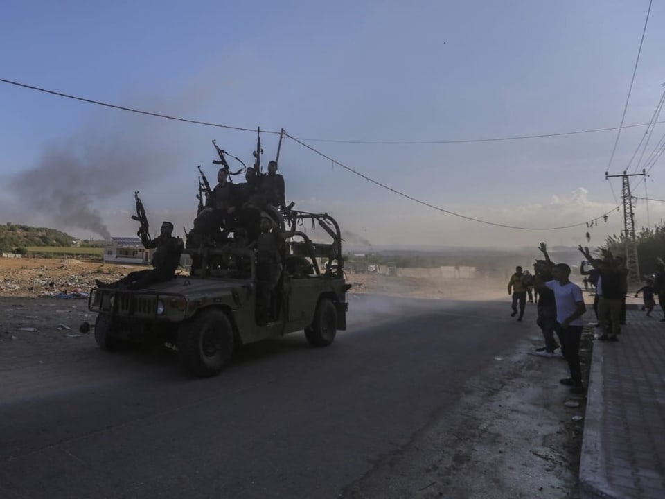 Militärjeep mit bewaffneten Personen und Zivilisten an einer staubigen Strasse