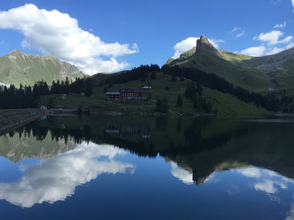Das Bergpanorama mit blauem Himmel und Wolken spiegelt sich in einem Bergsee.