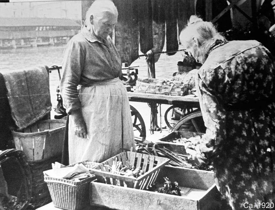 Marktstand mit Verkäuferin und einer Frau, die die Ware prüft. (Historisches schwarz-weiss Bild)