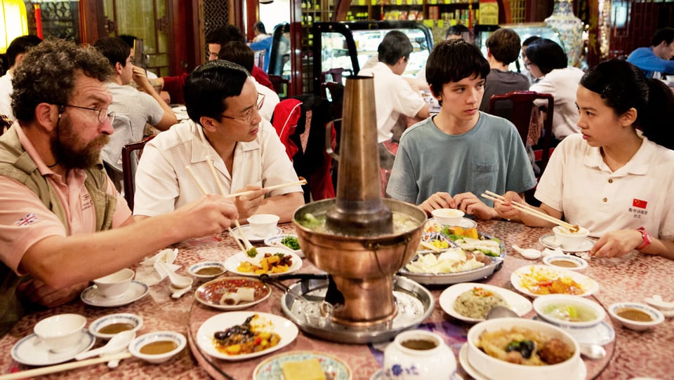 Vier Personen sitzen in einem Restaurant um einen runden Tisch und essen aus kleinen Schälchen.
