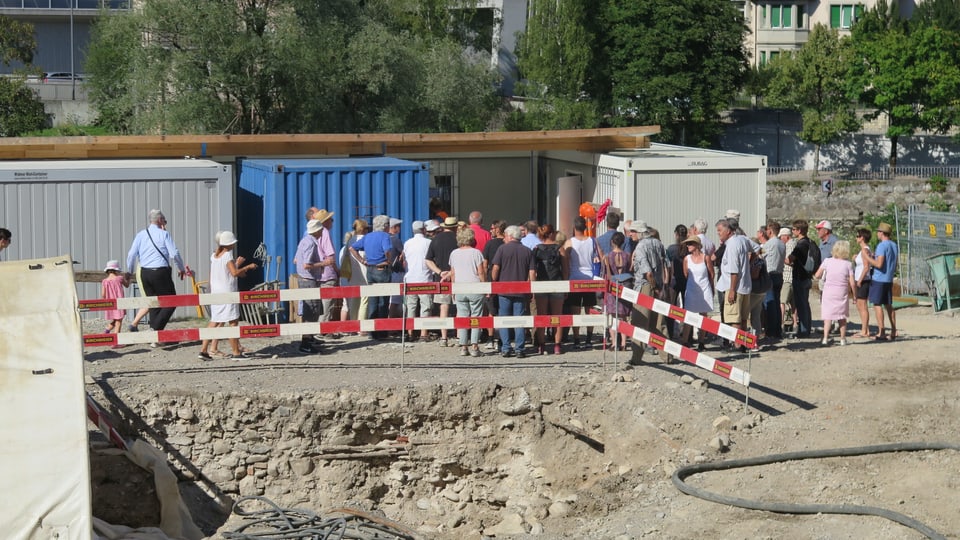 Eine Gruppe Besucher steht vor einem Baucontainer.