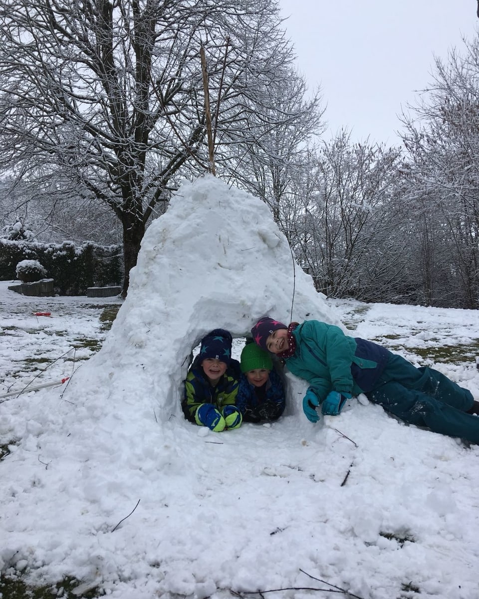 Drei Jungs haben einen Schneeberg gebaut mit einem Tunnel.