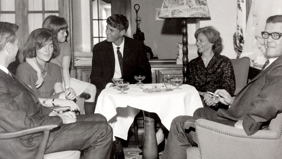 Eine Familie sitzt um ein Sofatischchen, auf dem Champagner-Gläser stehen.