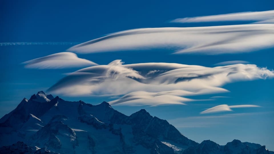 Linsenförmige Wolken am blauen Himmel über den Walliser Alpen. 