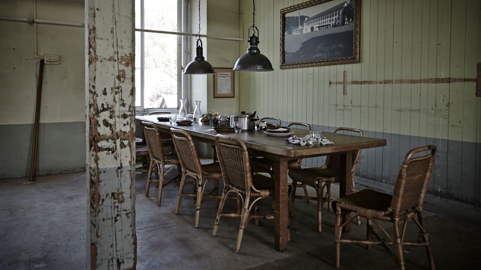 Mittagstisch Fabrik: Ein Tisch mit mehreren Stühlen in einem alten hohen Raum.