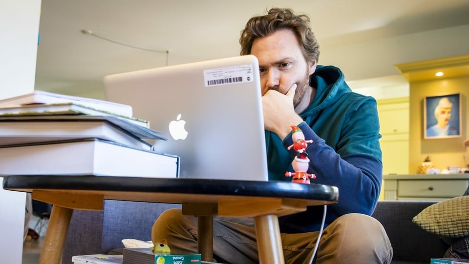Ein Mann sitzt zu Hause vor einem Laptop.