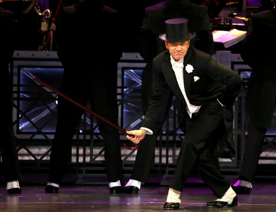 Mann im schwarzen Anzug tanzt auf Bühne. 