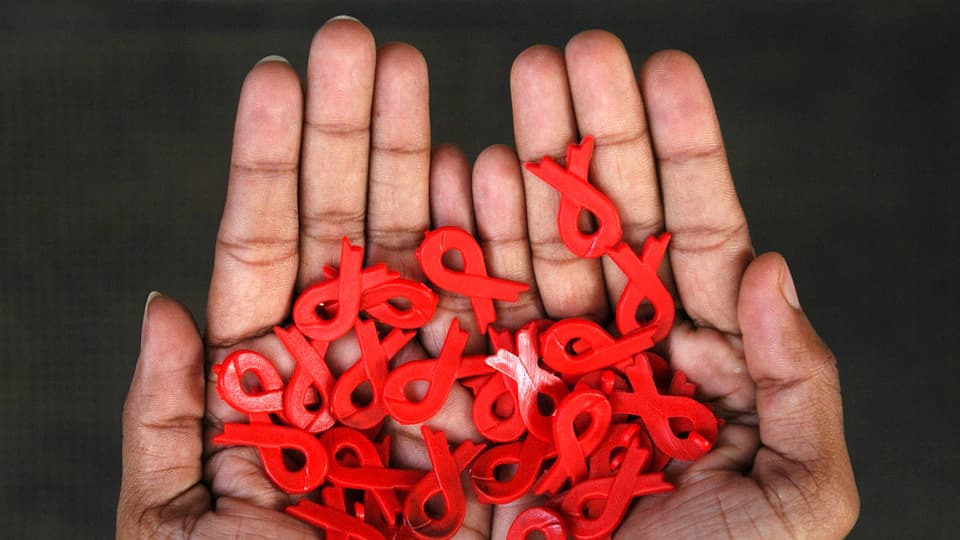 Eine Hand hält viele rote Schleifen – das Symbol für Aids.