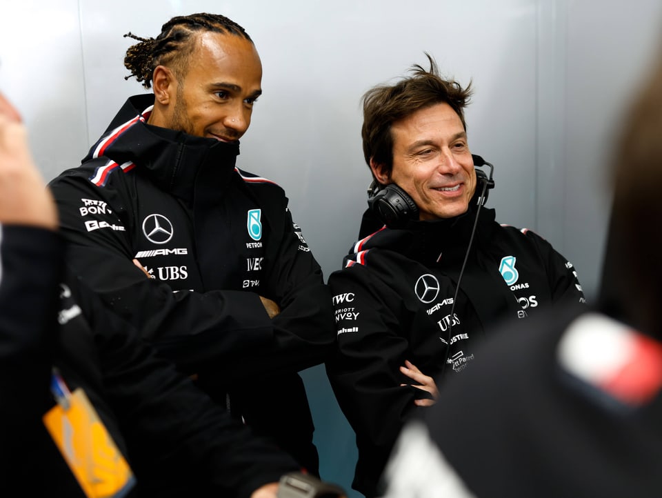 Lewis Hamilton und Toto Wolff stehen nebeneinander und grinsen schelmisch.