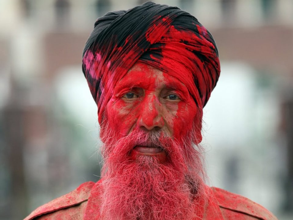 Ein Mann mit Bart und Turban ist mit roter Farbe verschmiert.