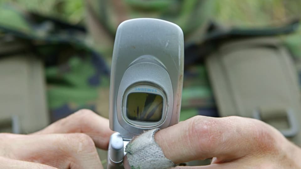 Ein Armeeangehöriger hält ein altes Handy in der Hand.