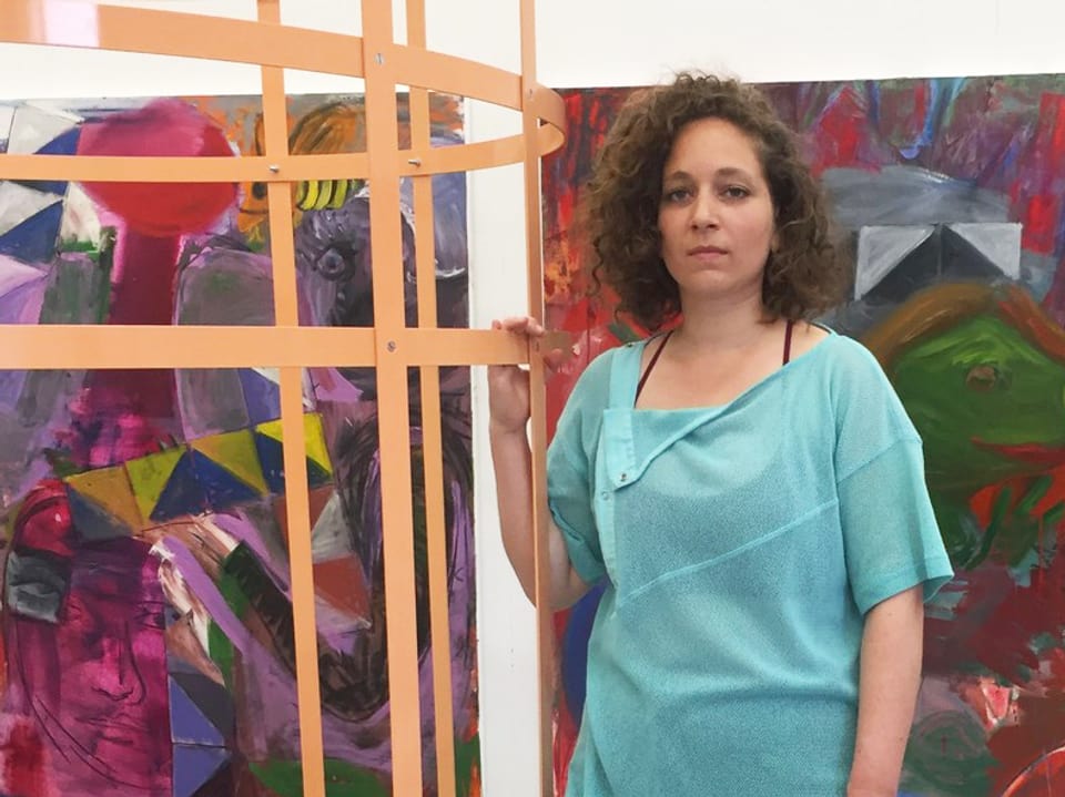 Sonia Kacem neben einem Kunstobjekt, im Hintergrund Bilder. 