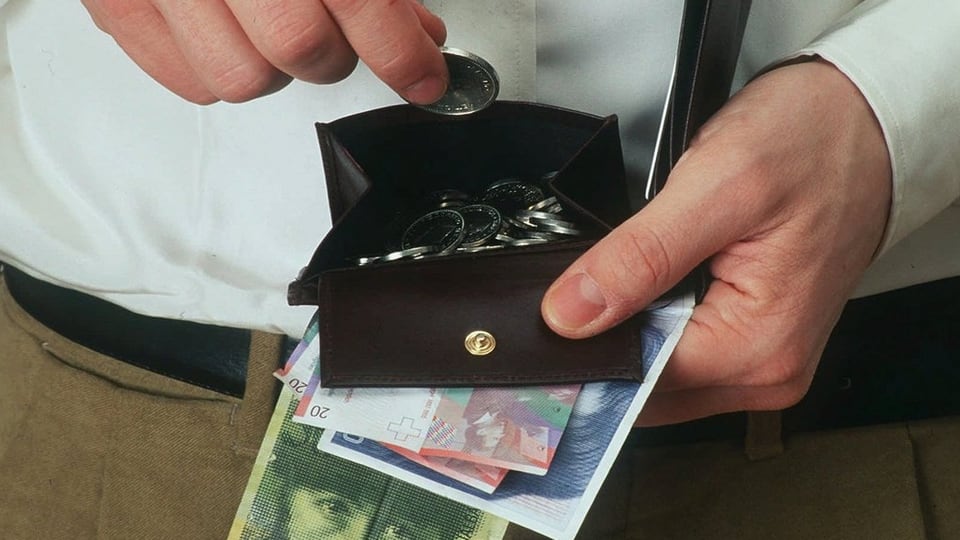 Ein Mann zieht eine Münze aus einem offenen Portemonnaie, Mehrere Banknoten hält er in der Hand.