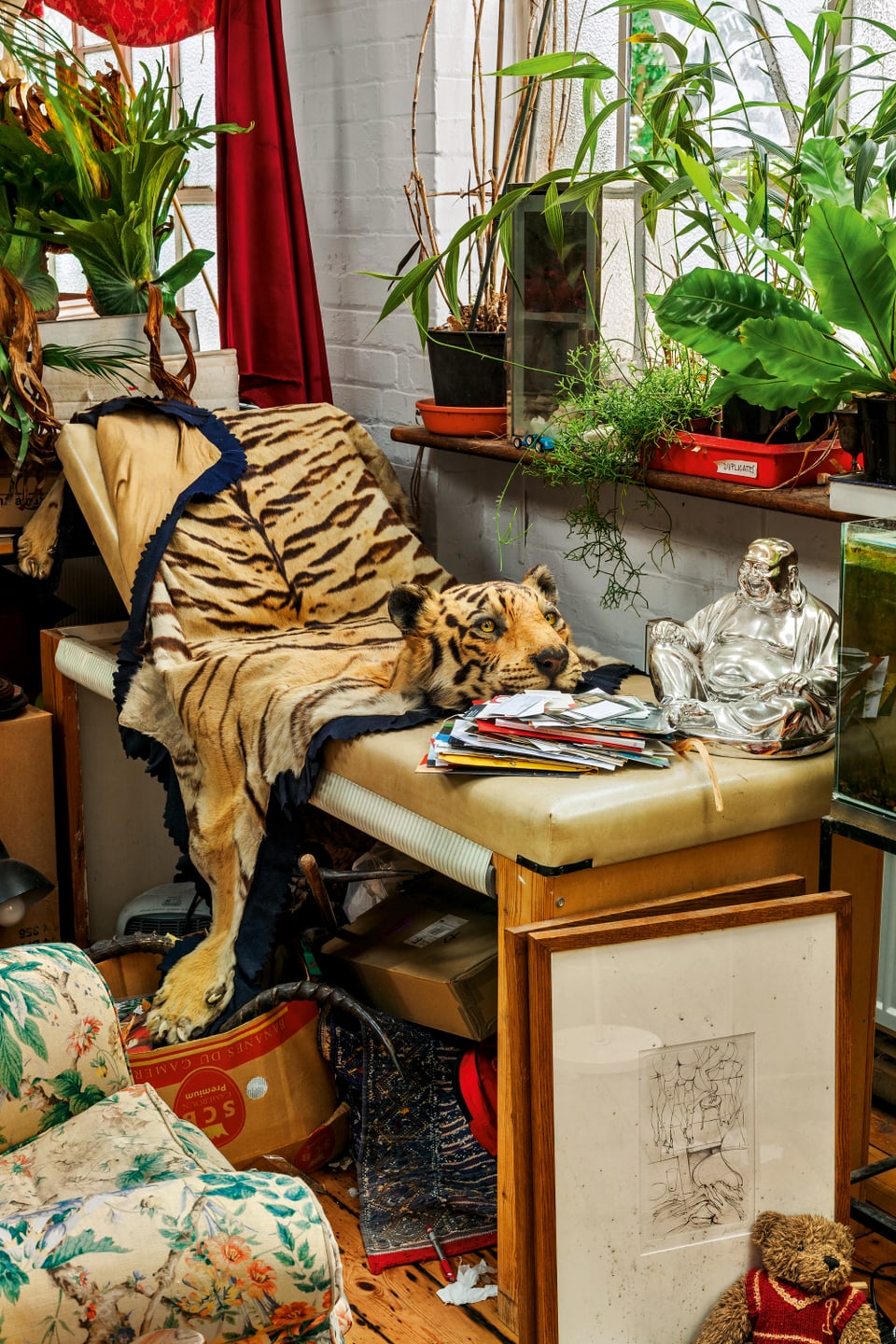 Neben einer Bank mit Tigerfell und Buddhastatue stehen verschiedene Pflanzen auf dem Fensterbrett.