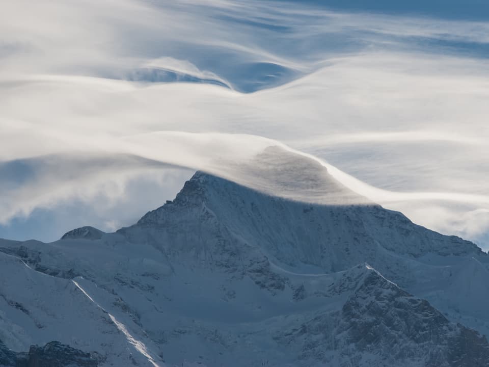 Ein Wolkenschleier legt sich im Form einer Welle über einen Alpengipfel.
