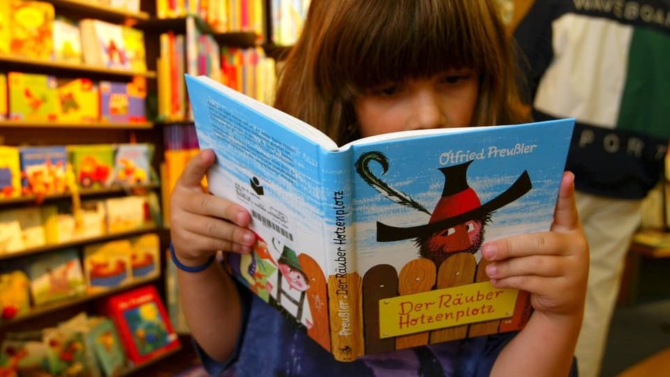 Ein kleines Mädchen liest im Buch «Der Räuber Hotzenplotz» von Ottfried Preussler.