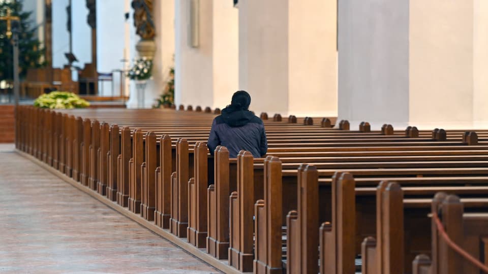 Eine Person sitzt alleine in einer Kirchen. 