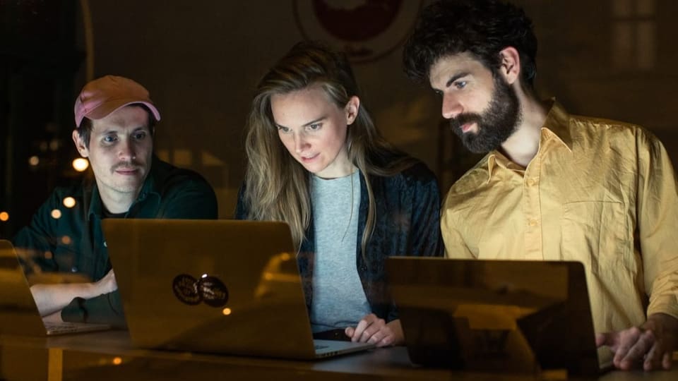 Zwei Männer und eine Frau sitzen konzentriert vor zwei Laptops.
