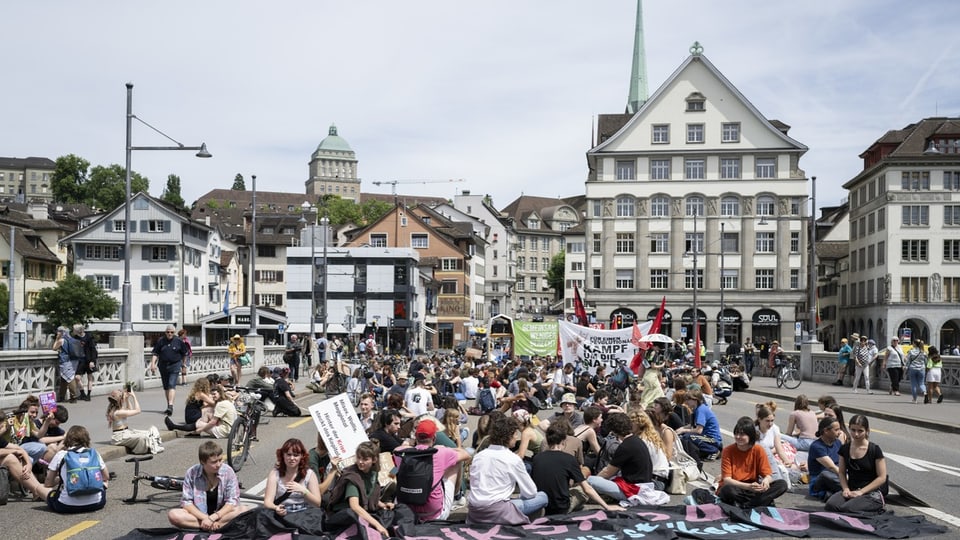 People sit on a bridge in the city with protest signs.
